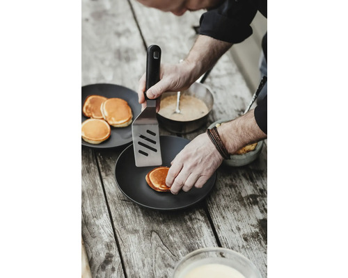 Eine Person wendet Pfannkuchen mit einem Pfannenwender auf einem Teller.