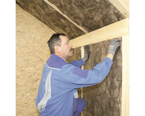 Ein Mann dämmt ein Haus mit Dämmwolle.