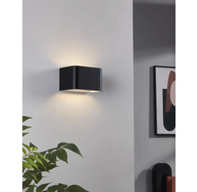 Schwarze würfelförmige Wandleuchte beleuchtet eine Wand