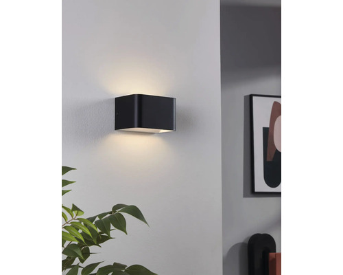 Schwarze würfelförmige Wandleuchte beleuchtet eine Wand