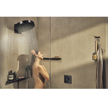 Frau unter einer Kopfbrause mit Handbrause und Ablage im modernen Duschraum