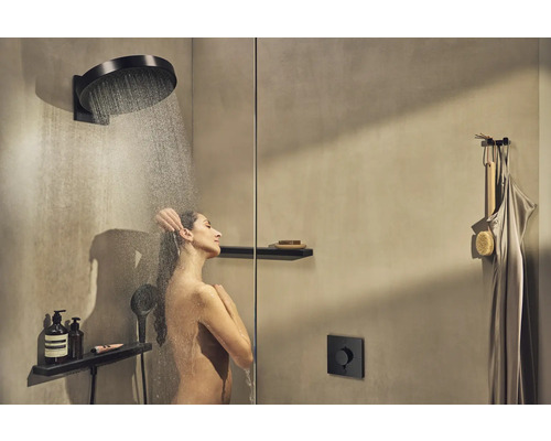 Frau unter einer Kopfbrause mit Handbrause und Ablage im modernen Duschraum