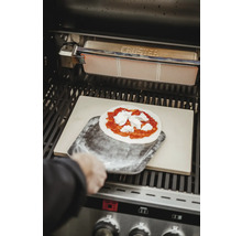 Pizza wird mit einem Pizzaschieber auf einen Pizzastein im Grill gelegt.