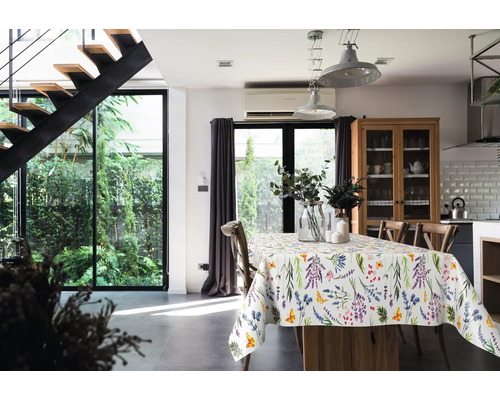 Heller Raum mit Esstisch, bedeckt mit einer Tischdecke mit Blumen- und Schmetterlingsmuster