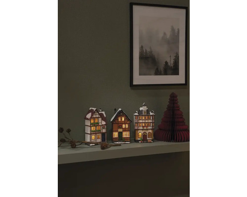 Dekorative Miniaturhäuser und ein Papierweihnachtsbaum auf einem Regal mit einem gerahmten Bild an der Wand