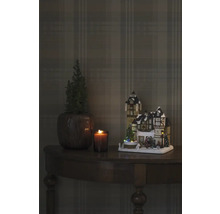 Dekorative Weihnachtsszene mit beleuchtetem Haus, Kerze und Pflanze auf einem Tisch