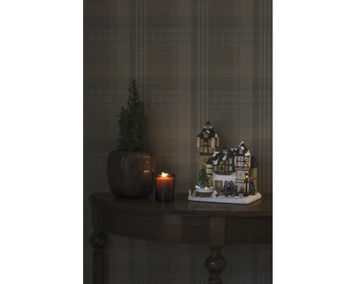 Dekorative Weihnachtsszene mit beleuchtetem Haus, Kerze und Pflanze auf einem Tisch