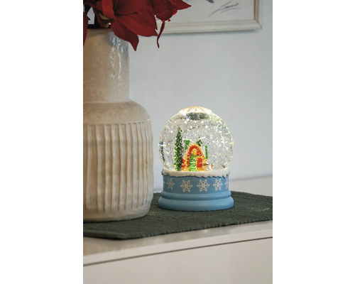 Schneekugel mit Haus und Tanne auf blauem Sockel mit Schneeflockenmuster