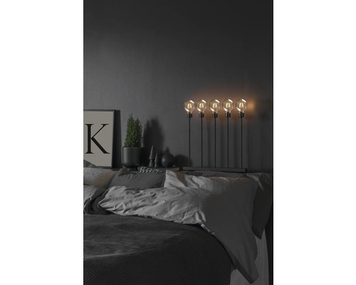 Dekoratives Schlafzimmer mit Bett, Nachttischlampe mit fünf Glühbirnen, Topfpflanze und Bild
