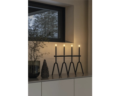 Dekoratives Arrangement mit einer schwarzen Leuchte mit vier Lichtern, einer kleinen Tanne und einem dekorativen Zweig in einem Interieur.