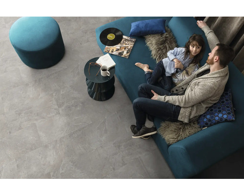 Wohnzimmer mit grauen Bodenfliesen in Steinoptik, Sofa, Hocker und Couchtisch
