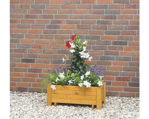Holzblumenkasten mit roter und weißer Bepflanzung vor einer Ziegelwand