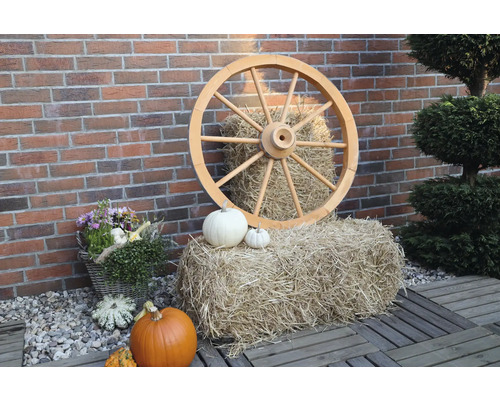 Dekorative Szene mit Holzrad, Strohballen und Kürbissen vor einer Ziegelmauer