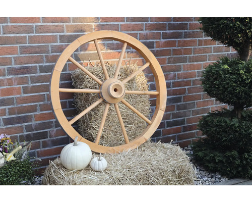 Dekoratives Wagenrad aus Holz vor einer Ziegelwand und Strohballen mit Kürbissen