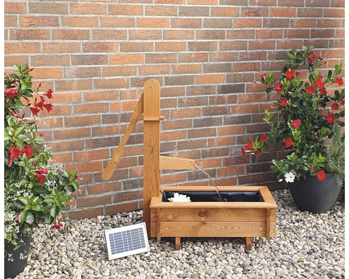 Gartenszene mit hölzernem Brunnen mit Solarpumpe und Pflanzgefäßen vor einer Backsteinmauer