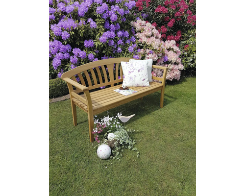 Gartenbank aus Holz mit Kissen vor blühenden Rhododendren