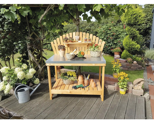 Gartenszene mit einem hölzernen Pflanztisch mit Metallplatte, dekoriert mit Pflanzen und Gartenzubehör.