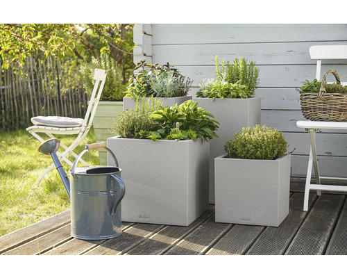 Drei quadratische Pflanzkübel mit Kräutern und eine Gießkanne im Garten