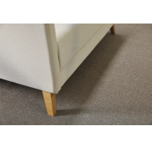 Detailansicht eines beigen Teppichbodens unter einem Sofa mit Holzfüßen