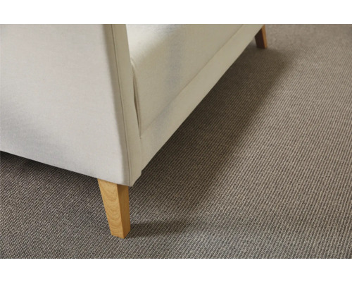 Detailansicht eines beigen Teppichbodens unter einem Sofa mit Holzfüßen