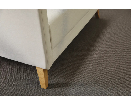 Detailansicht eines Sofas mit hellem Bezug und Holzfüßen auf einem Teppich