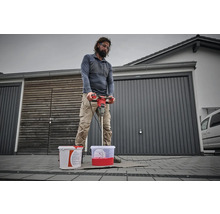 Mann mischt Farbe mit einem Farbmischer vor einer Garage