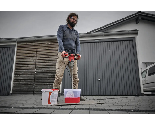 Mann mischt Farbe mit einem Farbmischer vor einer Garage