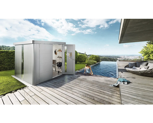 Modernes Gartenhaus neben einem Swimmingpool auf einer Holzterrasse. Im Inneren des Gartenhauses befindet sich ein Grill.