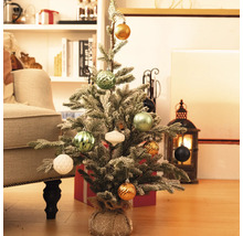 Dekorierter, kleiner Weihnachtsbaum auf dem Boden mit Geschenken und Dekorationen im Hintergrund.