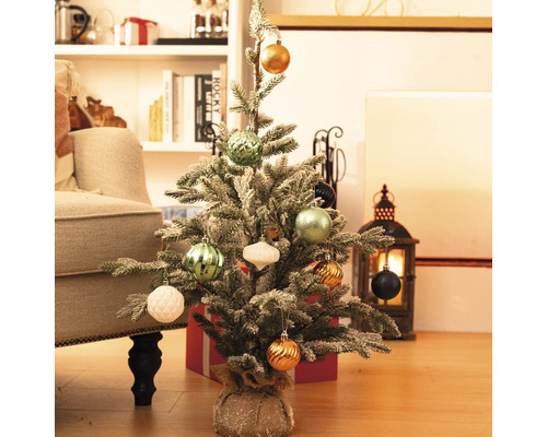 Dekorierter, kleiner Weihnachtsbaum auf dem Boden mit Geschenken und Dekorationen im Hintergrund.