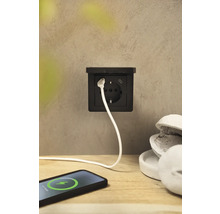 Eine schwarze Steckdose mit USB-Anschluss und ein Ladekabel, das mit einem Smartphone verbunden ist.