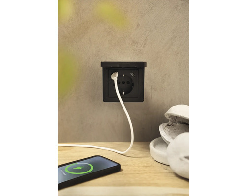 Eine schwarze Steckdose mit USB-Anschluss und ein Ladekabel, das mit einem Smartphone verbunden ist.