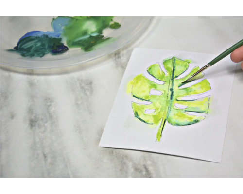 Aquarellmalerei eines Monstera-Blattes mit Pinsel und Farbpalette