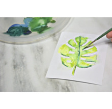 Aquarellmalerei eines Monstera-Blattes mit Pinsel und Farbpalette