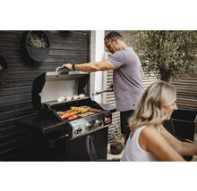 Mann grillt mit einem Gasgrill im Garten. Auf dem Grill liegen Gemüse und Fleisch.
