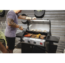 Mann grillt verschiedene Speisen auf einem Gasgrill im Freien.