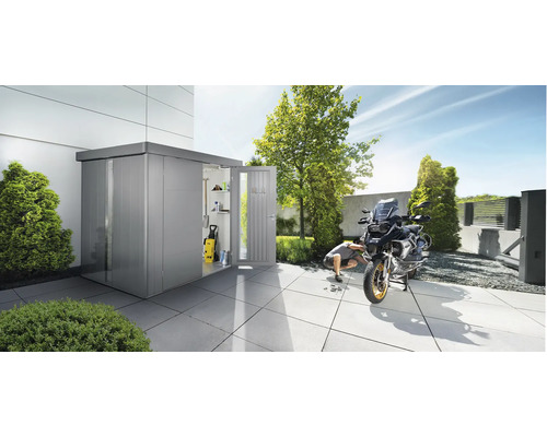 Szene im Garten mit Gerätehaus, in dem ein Hochdruckreiniger und Regale zu sehen sind. Ein Mann repariert ein Motorrad vor dem Gerätehaus.