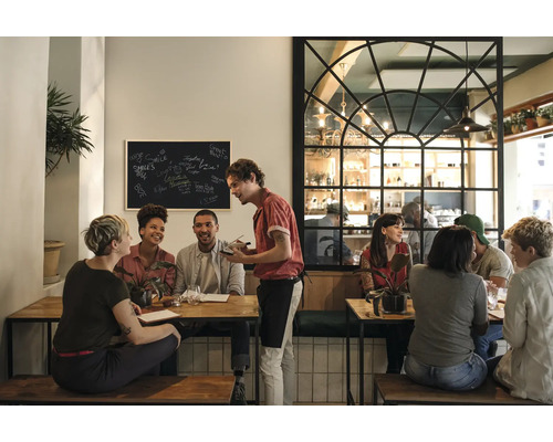 Szene in einem Restaurant mit Gästen an Tischen und einem Kellner, der Bestellungen aufnimmt.