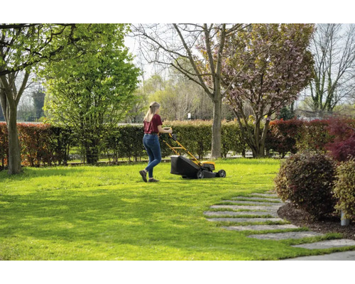 Frau mäht Rasen mit einem Rasenmäher in einem Garten.
