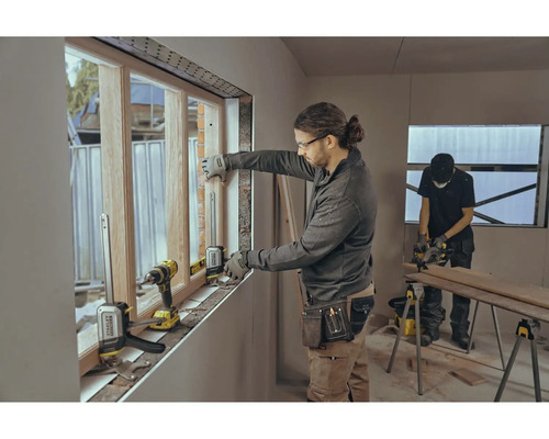 Zwei Handwerker montieren ein Fenster mit Werkzeugen in einem Rohbau.