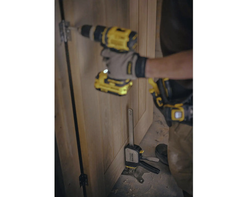 Ein Handwerker montiert mit einem Akkubohrer und einer Schraubzwinge ein Türscharnier an einer Holztür.