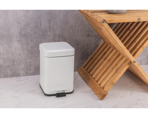 Weißer Treteimer aus Metall neben einem Holzschemel