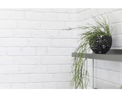 Dekorative Kunstpflanze in schwarzer Kugelvase auf einem Regal vor einer Ziegelwand