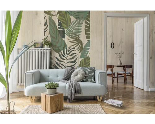 Wohnzimmer mit hellblauem Sofa, Holztisch, Zimmerpflanze und Wandtapete mit Blättermuster