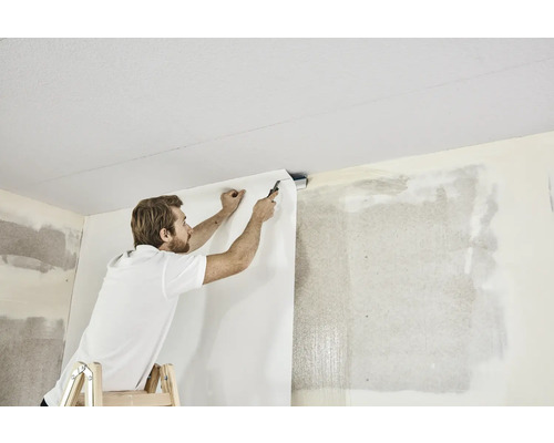 Mann auf Leiter befestigt Tapete an Wand