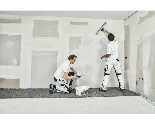 Zwei Handwerker verspachteln eine Wand in einem Raum.