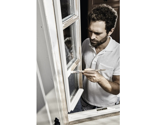 Ein Mann streicht mit einem Pinsel ein Fenster weiß.