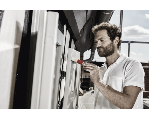 Mann streicht mit Pinsel Holzkonstruktion im Außenbereich