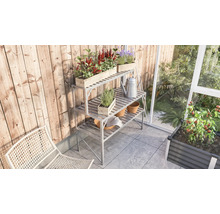 Gartenszene mit Pflanztisch, Pflanzen und Gartengeräten auf einer Terrasse neben einem Gewächshaus