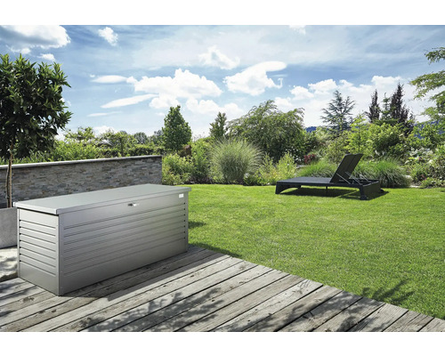 Gartenlandschaft mit einer Aufbewahrungsbox aus Metall und einer Sonnenliege auf einem Rasen